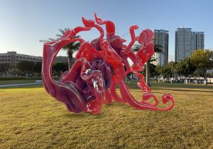 screen capture of AR sculpture on a grass field against high rise buildings