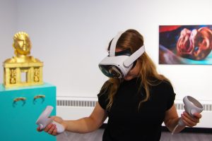 female wearing VR headset and holding controllers with sculpture and printed art in the background